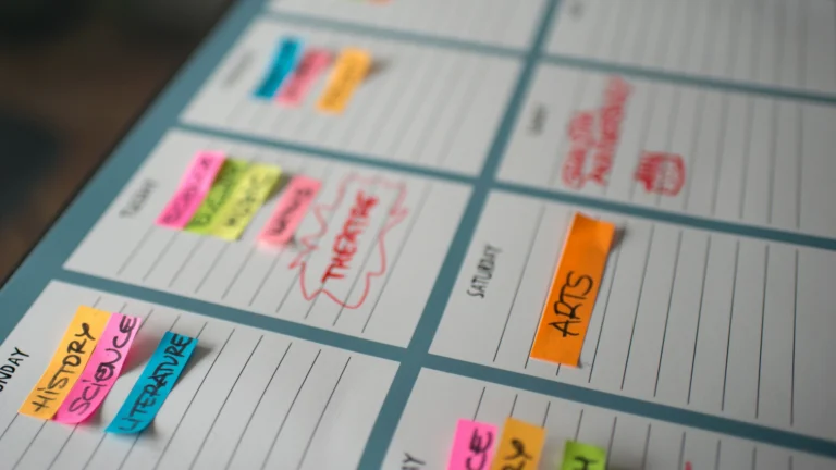 A weekly planner with colorful sticky notes labeling activities like SCIENCE, THEATRE, and ARTS. The planner has handwritten notes and is organized by day, with each section filled with vibrant reminders and tasks.