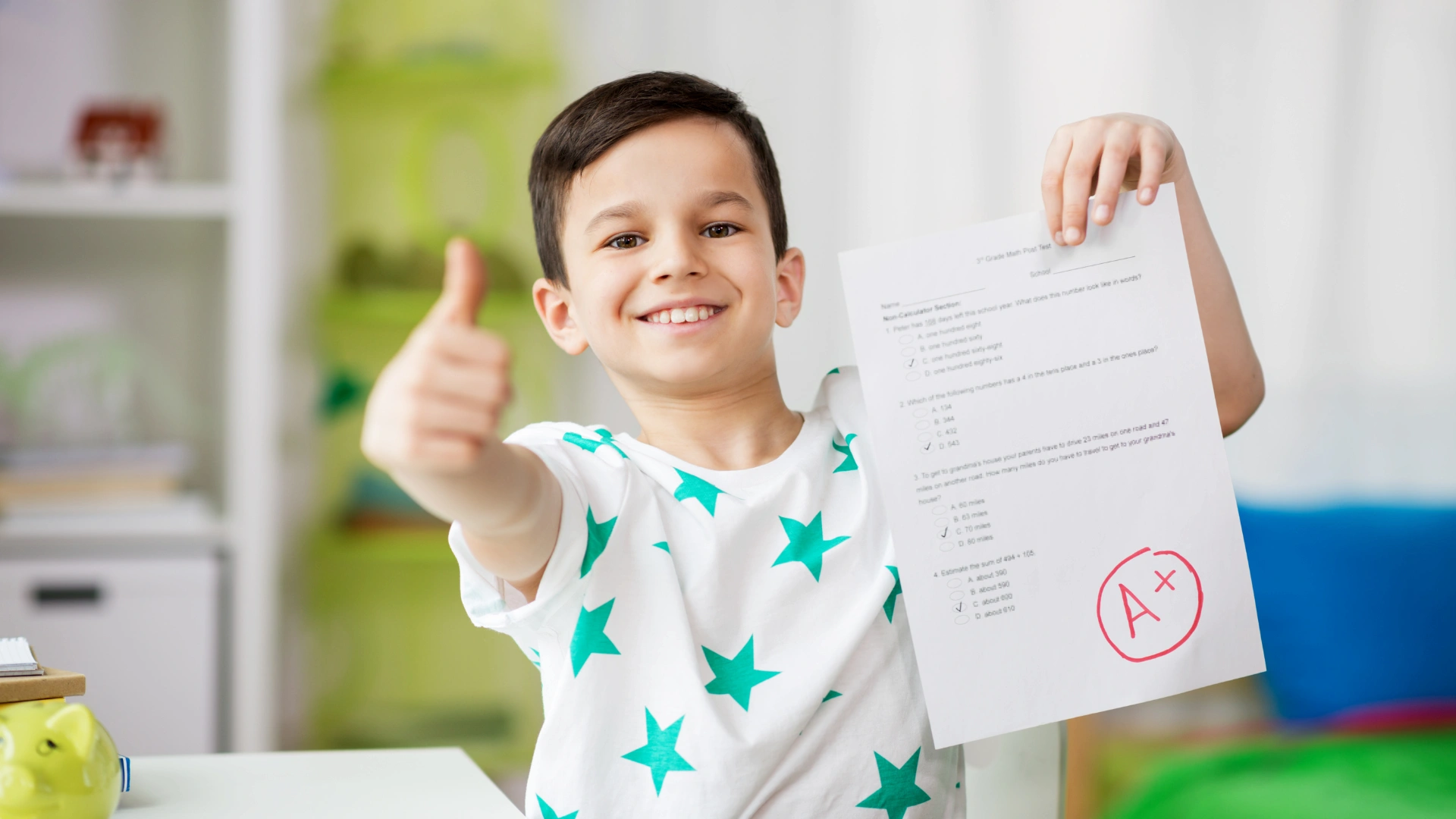 Smiling boy in a star-patterned shirt holds up a test paper with an A+ grade and gives a thumbs up in a bright room.