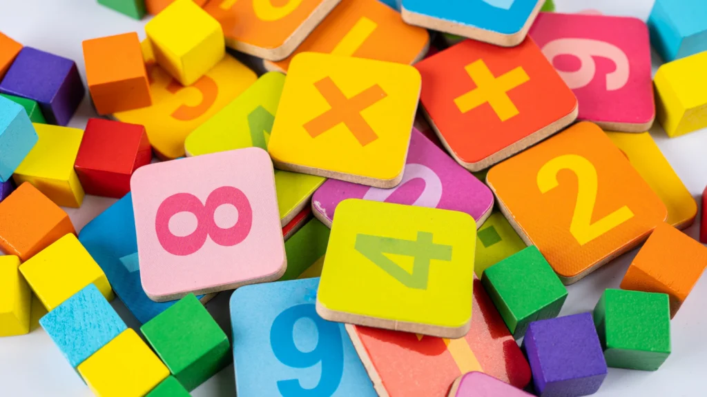 A colorful assortment of wooden blocks featuring numbers, plus signs, and squares, along with small multicolored cubes, ideal for real world math activities, scattered on a flat surface.