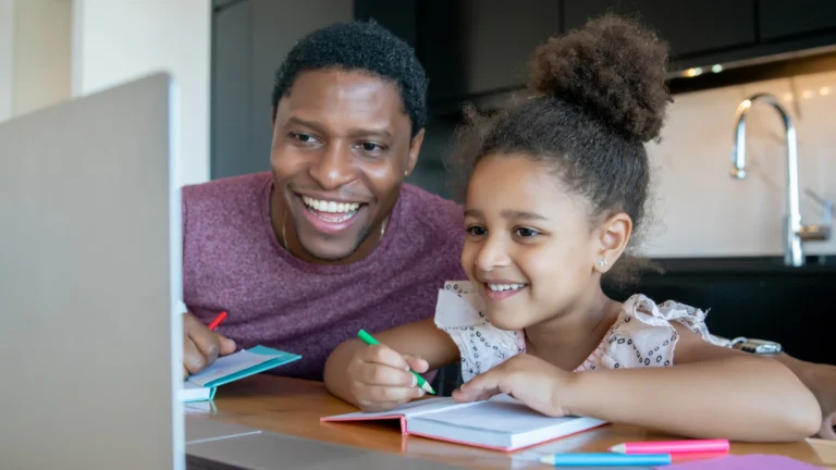 A smiling man and young girl sit at a table, looking at a laptop screen while writing in notebooks with colored pens, exploring whether DIY vs. Learning Hub resources work best for their creative projects.